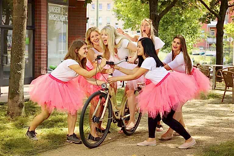 JGA Fotoshooting von Junggesellinnen im rosa Tütü die eine auf dem Fahrrad flüchtende Braut festhalten wollen