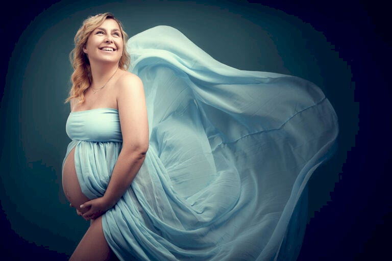 Fotoshooting einer schwangeren, glücklich lachenden, blonden Frau in einem türkis-blauem Kleid