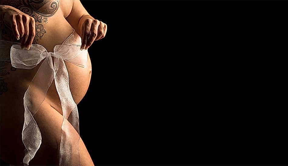 Foto einer Schwangeren Frau, die eine Schleife über ihrem Babybauch zurecht zieht